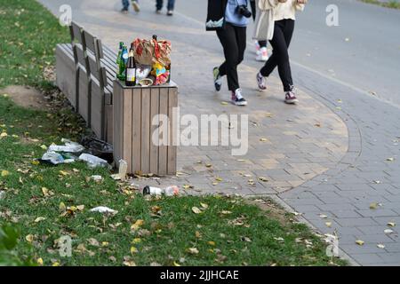Überfüllter Papierkorb auf der Straße. Müllkonzept. Haufen Plastikmüll auf Boden und Gras Stockfoto