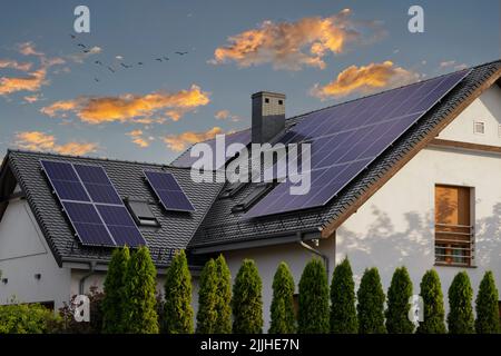 Großes, modernes Haus mit Sonnenkollektoren auf einem Schrägdach. Tageslicht bei Sonnenuntergang. Blaue Sonnenkollektoren. Stockfoto