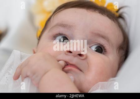 Schöne Latina Baby gelangweilt, liegend in ihrer Krippe, während Blick auf ihre Umgebung. Sechs Monate altes Mädchen berühren ihr Zahnfleisch mit dem Daumen. Stockfoto