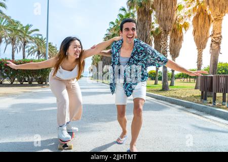 Junges, vielfältiges Paar mit Skateboard und Longboard, das Spaß im Freien hat. Stockfoto
