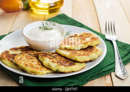 Vegane grüne Zucchini-Pfannkuchen in Teller und cremiger Sauce. Gesunde vegane Ernährung Lebensmittel auf Holz Hintergrund. Stockfoto