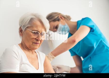 Junge Krankenschwester, die einer älteren grauhaarigen Frau im Krankenhaus Medikamente oder einen Anti-Covid-Impfstoff verabreicht. Hochwertige Fotos Stockfoto