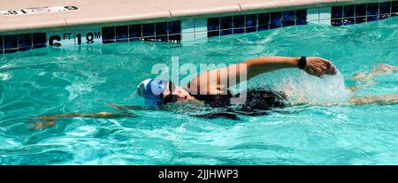 Seitenansicht einer Frau, die in einem Hotelpool Freistil-Bahnen schwimmt. Stockfoto
