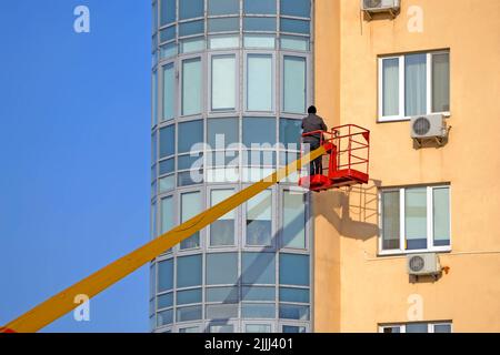 Unbekannter Mann in roter Konstruktion Wiege Befestigung des Glasfensters auf dem Gebäude in Kiew, Ukraine. Stockfoto