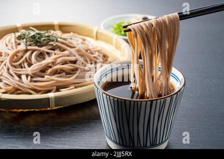 Zaru-soba auf schwarzem Hintergrund platziert. Soba-Nudeln in Nudelsuppe getaucht. Zaru Soba ist ein traditionelles japanisches Essen. Stockfoto