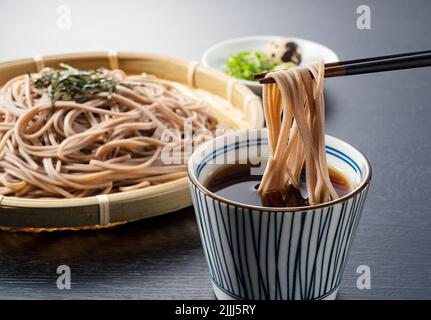 Zaru-soba auf schwarzem Hintergrund platziert. Soba-Nudeln in Nudelsuppe getaucht. Zaru Soba ist ein traditionelles japanisches Essen. Stockfoto