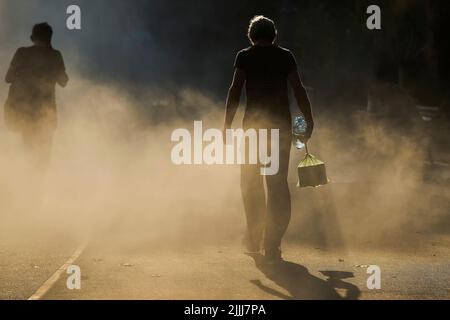 Bukarest, Rumänien - 26. Juli 2022: Ein Mann mit einer Wasserflasche läuft an einem sehr heißen Tag durch den feinen Sprühnebel eines Brunnens Dieses Bild ist für Eito Stockfoto