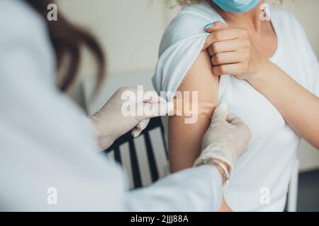 Arzt mit Gummischutzhandschuhen, der nach der Impfung einen Haftverband auf den Arm des Patienten legt. Pandemieprävention. Coronavirus-Impfung Stockfoto