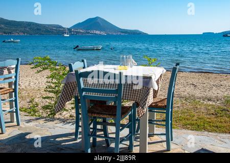 Typisch griechischer Tavernentisch am Meer mit Holzstühlen an der Küste von Gialova in der Nähe von Pylos, Messinia, Griechenland, Europa Stockfoto