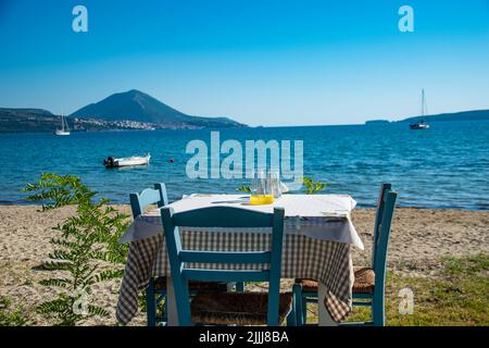 Typisch griechischer Tavernentisch am Meer mit Holzstühlen an der Küste von Gialova in der Nähe von Pylos, Messinia, Griechenland, Europa Stockfoto
