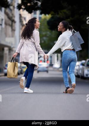 Zwei Cutys machen sich den Weg die Straße hinunter. Zwei Freunde gehen fröhlich die Straße entlang, nachdem sie den Tag mit Einkaufen verbracht haben. Stockfoto