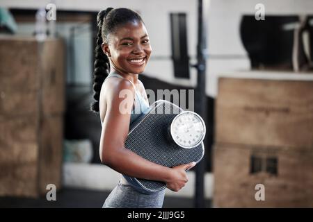 Machen Sie sich stolz. Eine fit junge Frau mit einer Waage, während im Fitnessstudio. Stockfoto