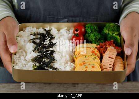 Dosirak oder Doshirak, nach koreanischem Stil verpackte Mahlzeit Bento Lunchbox mit verschiedenen Banchan, Gyeran Mari, Tomate, Brokkoli, Kimchi, Und Wurst. Weibliche Kinder Hol Stockfoto