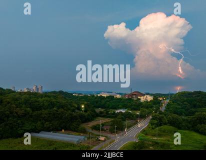 In der Abenddämmerung trifft ein Blitz die Straße von einer aufragenden Wolke über dem Land Stockfoto