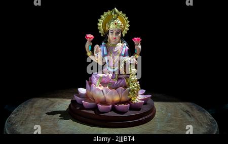 Hindu-Kosmos Maha laxshmi Statue mit Blumengirlande auf schwarzem Hintergrund verziert. Statue der Göttin des Reichtums, Kopierraum, selektiver Fokus. Stockfoto