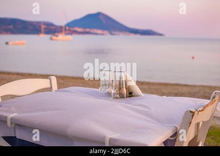 Typisch griechischer Tavernentisch am Meer mit Holzstühlen an der Küste von Gialova in der Nähe von Pylos, Messinia, Griechenland, Europa Stockfoto