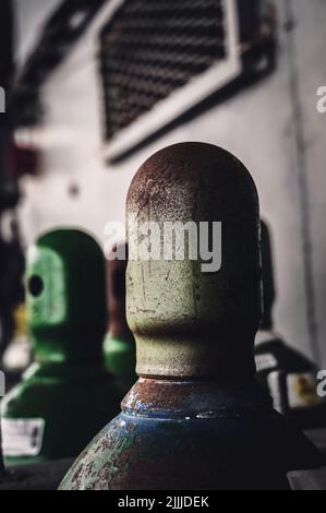 Druckgasflaschen, die vertikal durch eine Metallkette und eine Metallkappe gesichert gelagert werden. Stockfoto