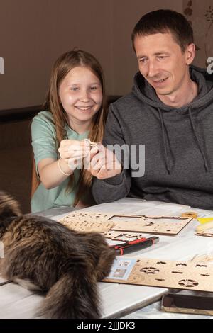 Erwachsene Mann Teenager-Tochter Spaß zusammen mit Holz arbeiten, DIY Hausaufgaben-Projekt. Kind und Vater lächelt und schaut auf hölzerne Details. Vater Stockfoto