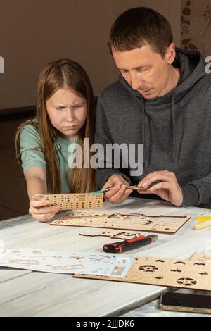 Erwachsener Mann, der Tochter im Teenageralter beibringt, mit Holz zu arbeiten. Ernsthaftes Kind und Vater schauen sich Anweisungen und hölzerne Details an. Konzentrierter Vater und Tochter Stockfoto