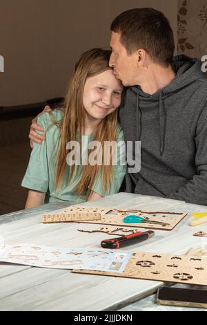 Papa und Teenager-Tochter arbeiten zusammen an Heimwerker-Hausaufgaben-Projekt. Papa umarmt und küsst lächelnde Tochter. Glückliches Familienkonzept. Vatertag Freundschaft da Stockfoto