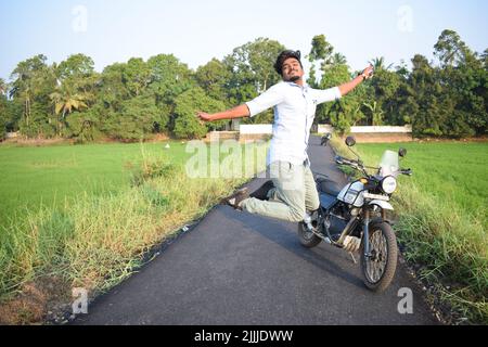 Ein Mann springt und posiert für Foto mit Motorrad in der Nähe von Reisfeld Stockfoto