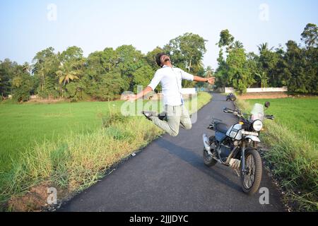 Ein Mann springt und posiert für Foto mit Motorrad in der Nähe von Reisfeld Stockfoto