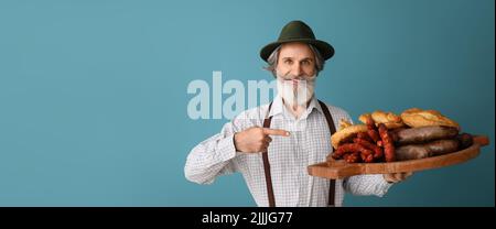 Hübscher Mann in traditioneller deutscher Kleidung und mit Snacks auf blauem Hintergrund mit Platz für Text Stockfoto