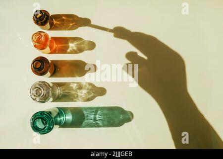 Serum mit Kollagen und Peptiden in bunten Glasflaschen auf beigem Hintergrund mit Sonnenschatten. Hautpflegeessenz für schöne, gesunde Haut. Oben Stockfoto