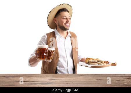 Schöner Mann in traditioneller deutscher Kleidung, mit Snacks und Bier am Tisch auf weißem Hintergrund Stockfoto