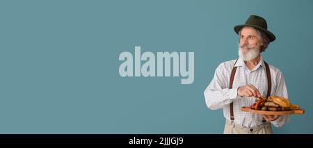 Schöner reifer Mann in traditioneller deutscher Kleidung und mit Snacks auf blauem Hintergrund mit Platz für Text Stockfoto