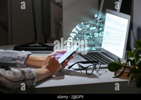 Frau mit Telefon und Laptop am Tisch am Abend. Konzept der Aktualisierung Stockfoto