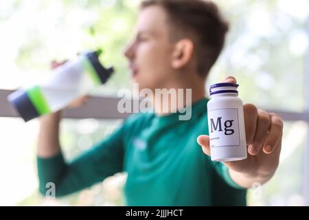 Junger Mann mit einer Flasche Magnesiumtabletten und Trinkwasser in der Nähe des Fensters, Nahaufnahme Stockfoto