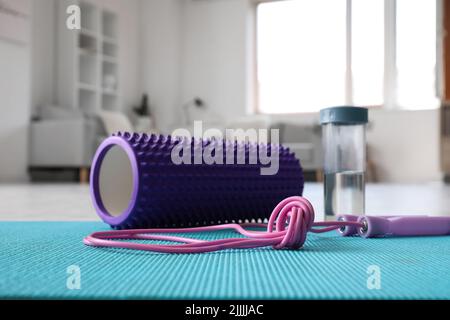 Schaumstoffrolle mit Springseil und Wasserflasche auf Matte im Wohnzimmer Stockfoto