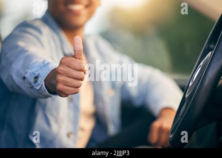 Ich brauche ein Taxi, kenne einen Typen, einen nicht erkennbaren Mann, der den Daumen hoch zeigt, während er in einem Auto unterwegs ist. Stockfoto