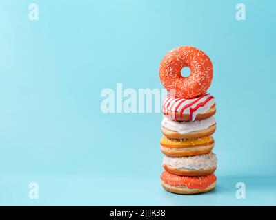 Stapel von verschiedenen Donuts auf blauem Hintergrund. Viele bunte glasierte Donuts mit Streuseln, die mit Kopierraum übereinander gestapelt sind Stockfoto