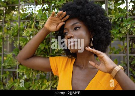 Porträt einer schönen jungen afroamerikanischen Frau, die vor dem Hintergrund einer grünen Hecke posiert Stockfoto