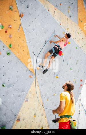 Weibliche Fitness-Profi Sportkletterin, die trainiert, von einem männlichen Lehrer abgesetzt. Stockfoto