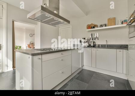 Beleuchtete Schränke mit Waschbecken und Geräten befinden sich in einer geräumigen, hellen Küche in einer modernen Wohnung Stockfoto