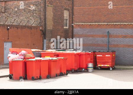 Seitenansicht auf einer Reihe roter Recycling-Behälter entlang einer Backsteinmauer in einer Stadtgasse, mit Platz für Text oben Stockfoto