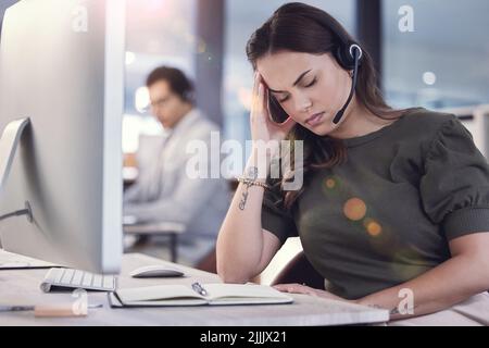 Ich glaube, ich brauche eine Pause, eine junge Callcenter-Agentin, die bei der Arbeit unter Kopfschmerzen leidet. Stockfoto