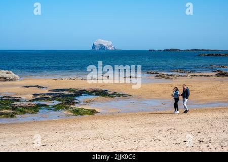 Junges Paar, das am Milsey Bay Beach mit dem Bass Rock in der Ferne, North Berwick, East Lothian, Schottland, Großbritannien, die Frühlingssonne genießt Stockfoto