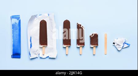 Schokoladenüberzocktes Eis auf Holzstäbchen bei verschiedenen Zuständen des Lebenszyklus des Verbrauchs auf blauem Hintergrund Draufsicht flaches Lay Stockfoto
