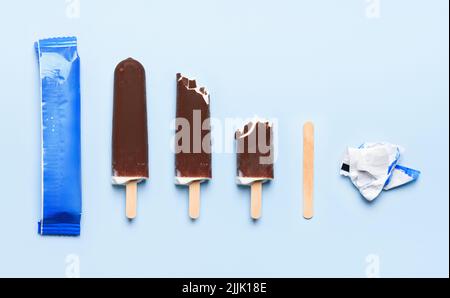 Schokoladenüberzocktes Eis auf Holzstäbchen bei verschiedenen Zuständen des Lebenszyklus des Verbrauchs auf blauem Hintergrund Draufsicht flaches Lay Stockfoto