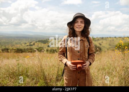 Lächelnde weibliche Reisende posiert und hält Fotokamera auf Safari Stockfoto