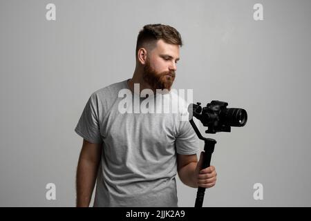 Videofilmer, der mit Steadicam gute Aufnahmen macht. Kameramann Schöpfer mit einem Stabilisator in den Händen nimmt ein Video auf der slr-Videokamera auf weiß Stockfoto