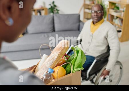 Nahaufnahme eines Freiwilligen, der eine Einkaufstasche aus Papier mit Lebensmitteln für einen Menschen mit Behinderung in sein Haus trägt Stockfoto