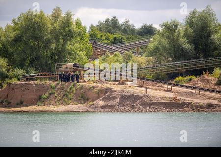 Porta Westfalica, Deutschland. 27.. Juli 2022. Polizisten stehen am Rand des Schotterteiches, wo zwei Personen am Sonntag (24.07.2022) aus unerklärlichen Gründen beim Schwimmen nicht an die Oberfläche kamen. Nach Angaben eines Feuerwehrsprechers sind einige Teile des Sees etwa 30 Meter tief. Experten der Polizei wollen nun mit einer Unterwassersonde nach den beiden Menschen suchen. Quelle: Lino Mirgeler/dpa/Alamy Live News Stockfoto