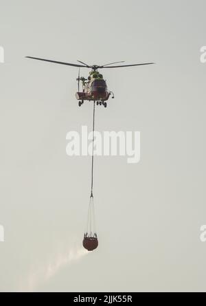 Helikopter von INFOCA mit einem Wassereimer, der auf ein Waldfeuer fällt, Mijas, Spanien. Stockfoto