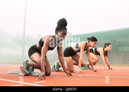 Wer gewinnt. In voller Länge eine Gruppe attraktiver junger Sportlerinnen, die auf der Strecke ihre Startpositionen einnehmen. Stockfoto