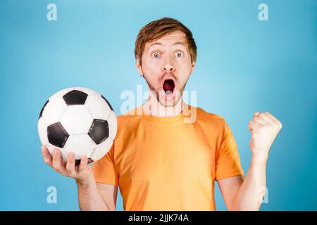 Begeisterter junger Mann, der einen Fußball hält und den Sieg eines Fußballspiels feiert. Stockfoto